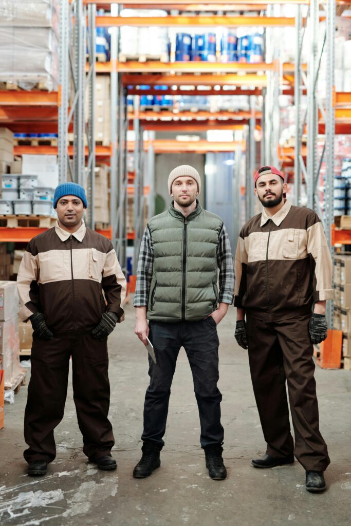 Three warehouse workers in uniform standing confidently in an organized storage area.